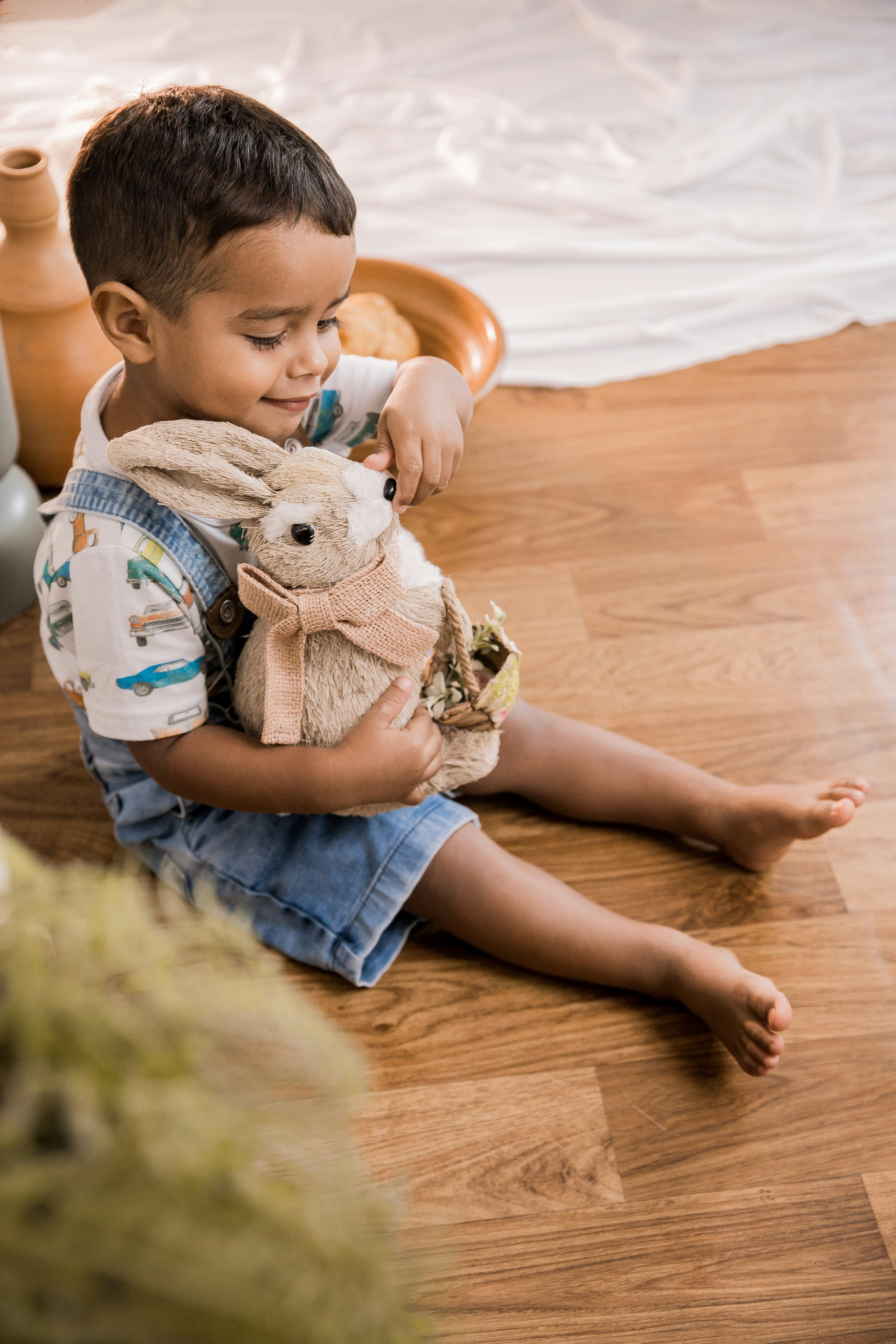 boy in blue denim shorts sitting on floor holding white rabbit plush toy